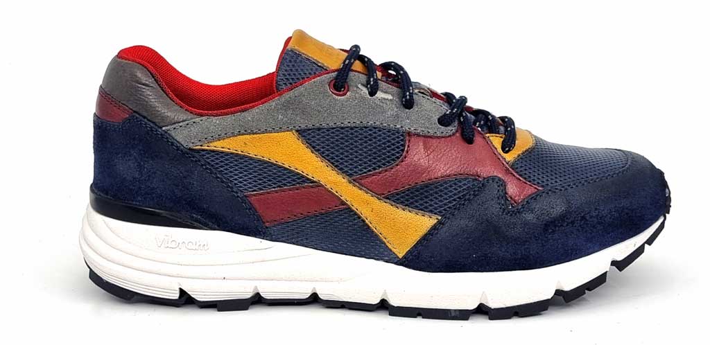 A close-up shot of the external side of the Exton Rocco sneaker, showcasing its premium blue leather upper with perforated detailing for breathability. The sneaker features eye-catching accents in yellow, grey, and red, adding a bold and modern touch. The lace-up closure is visible, ensuring a snug fit, while the padded collar offers extra comfort. The sleek design highlights Italian craftsmanship with precise stitching and high-quality materials.